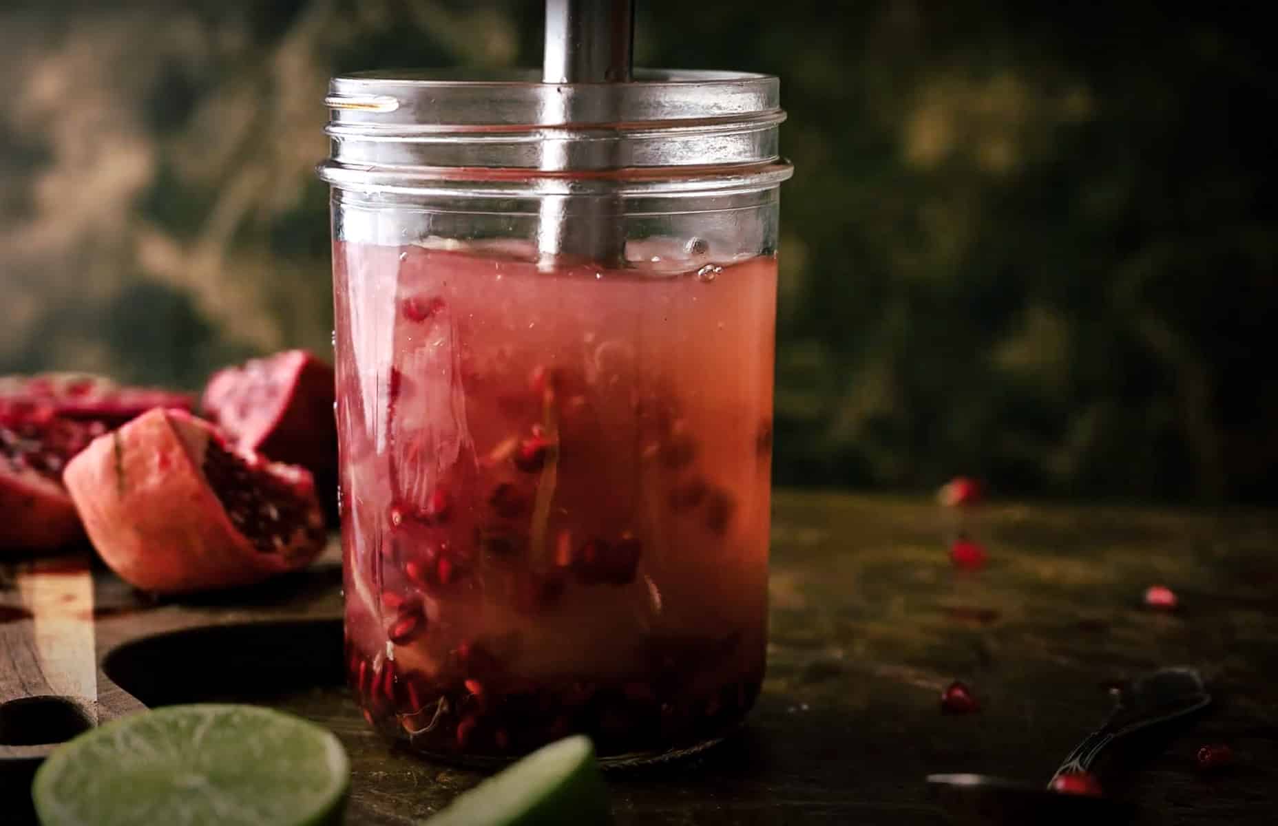 A glass mason jar filled with pomegranate seeds and juice being blended.