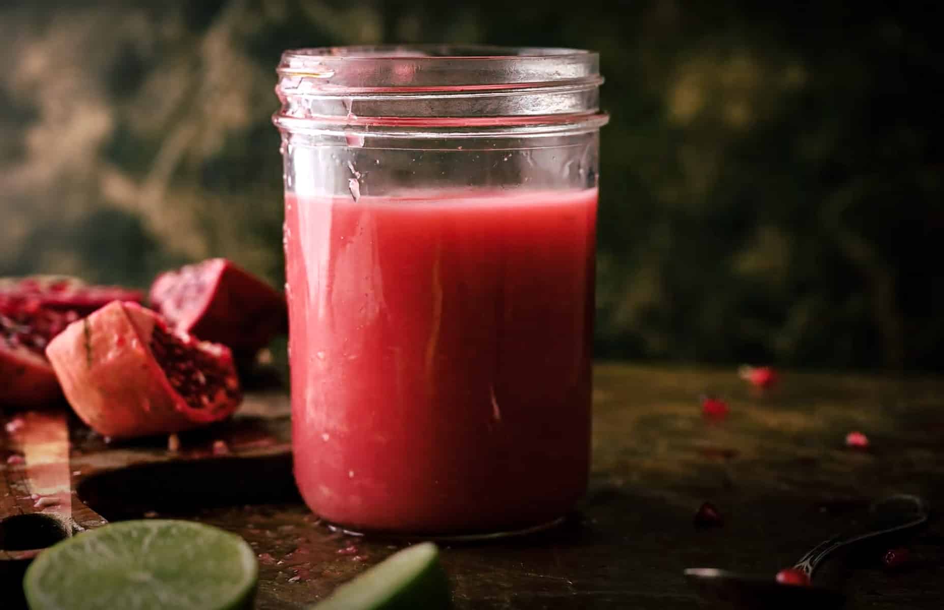 A glass jar filled with a pinkish-red juice is placed on a dark wooden surface.