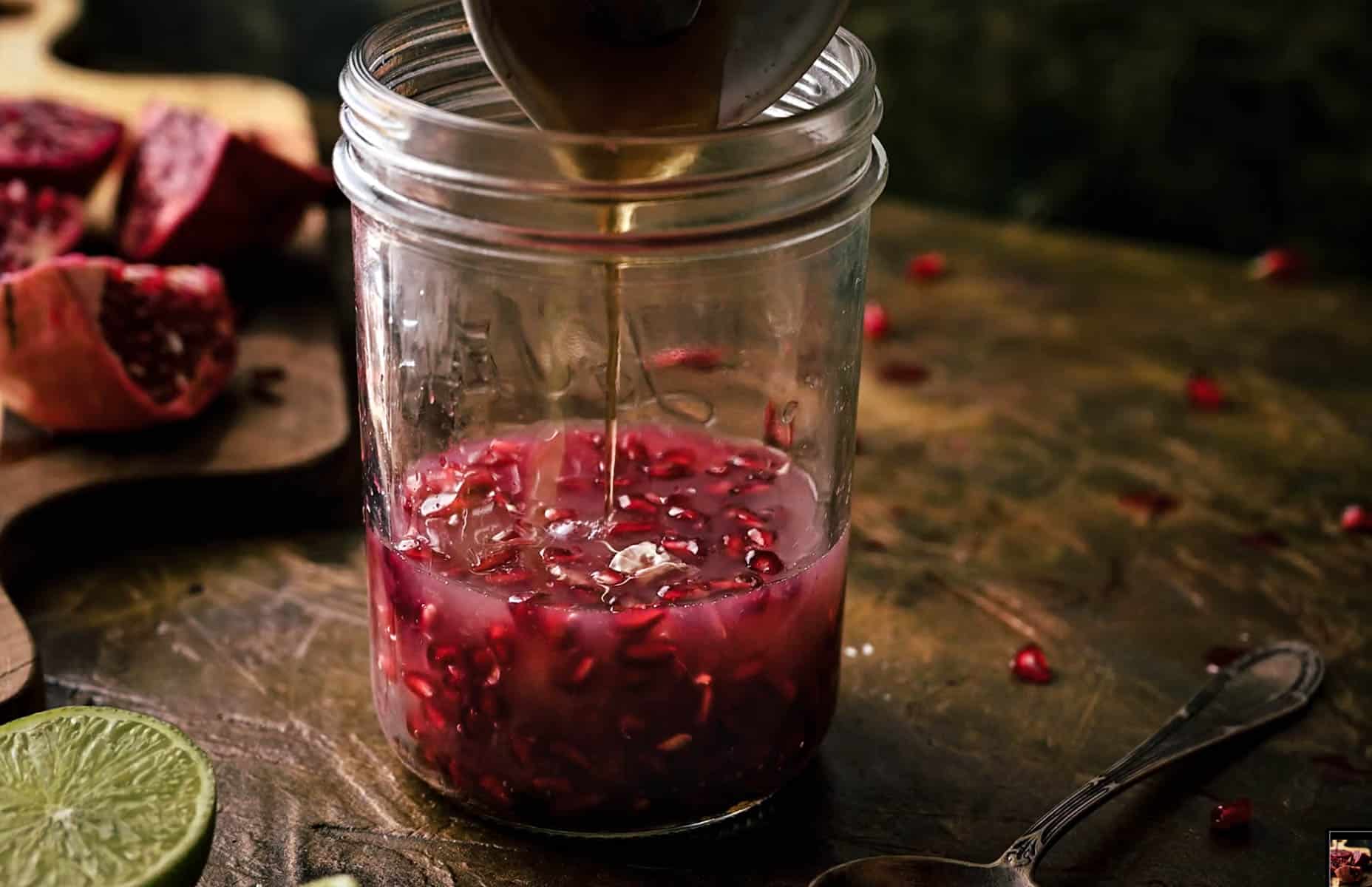 Close-up of a glass jar filled with pomegranate seeds and juice, as maple syrup is being poured in.
