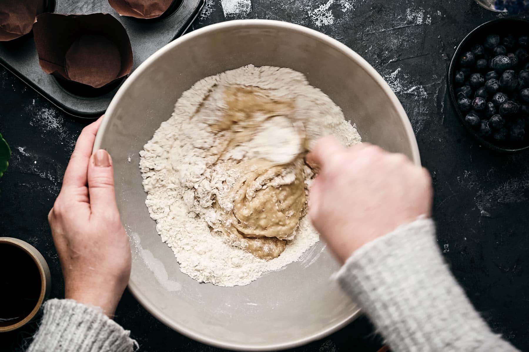 Hands mixing batter with flour in a bowl.