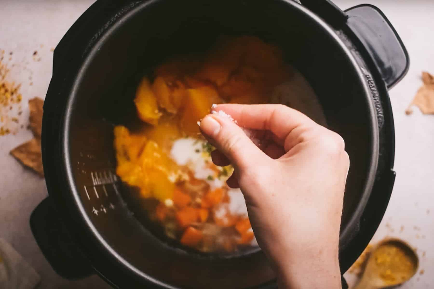 A hand is sprinkling salt into a pot containing a mix of vegetables and other ingredients.