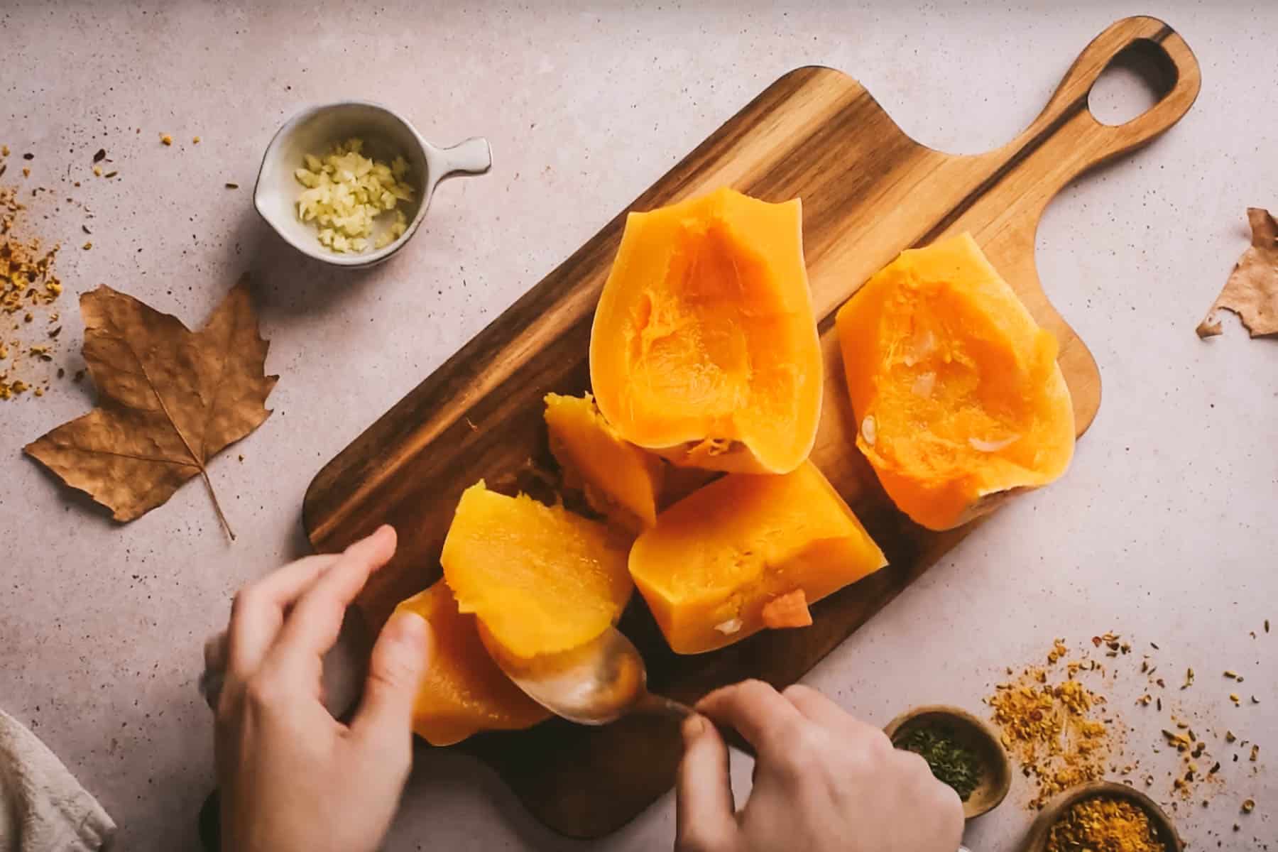 Person scooping seeds out of halved butternut squash on a wooden cutting board.