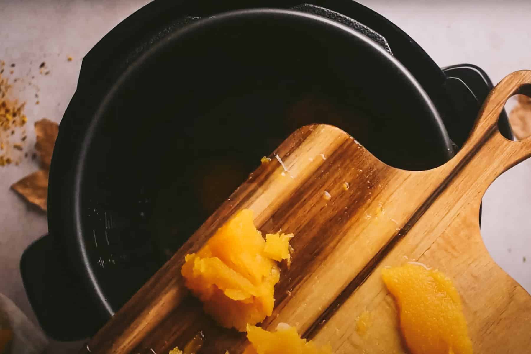 An electric cooker with peeled squash chunks being transferred from a wooden cutting board.