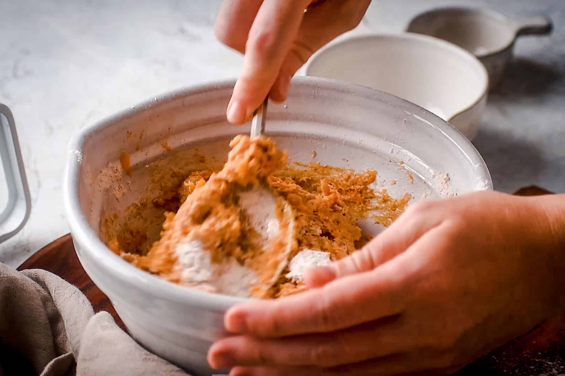 Hands mixing batter in a white ceramic bowl with a spoon, showing a close-up of the scone preparation.