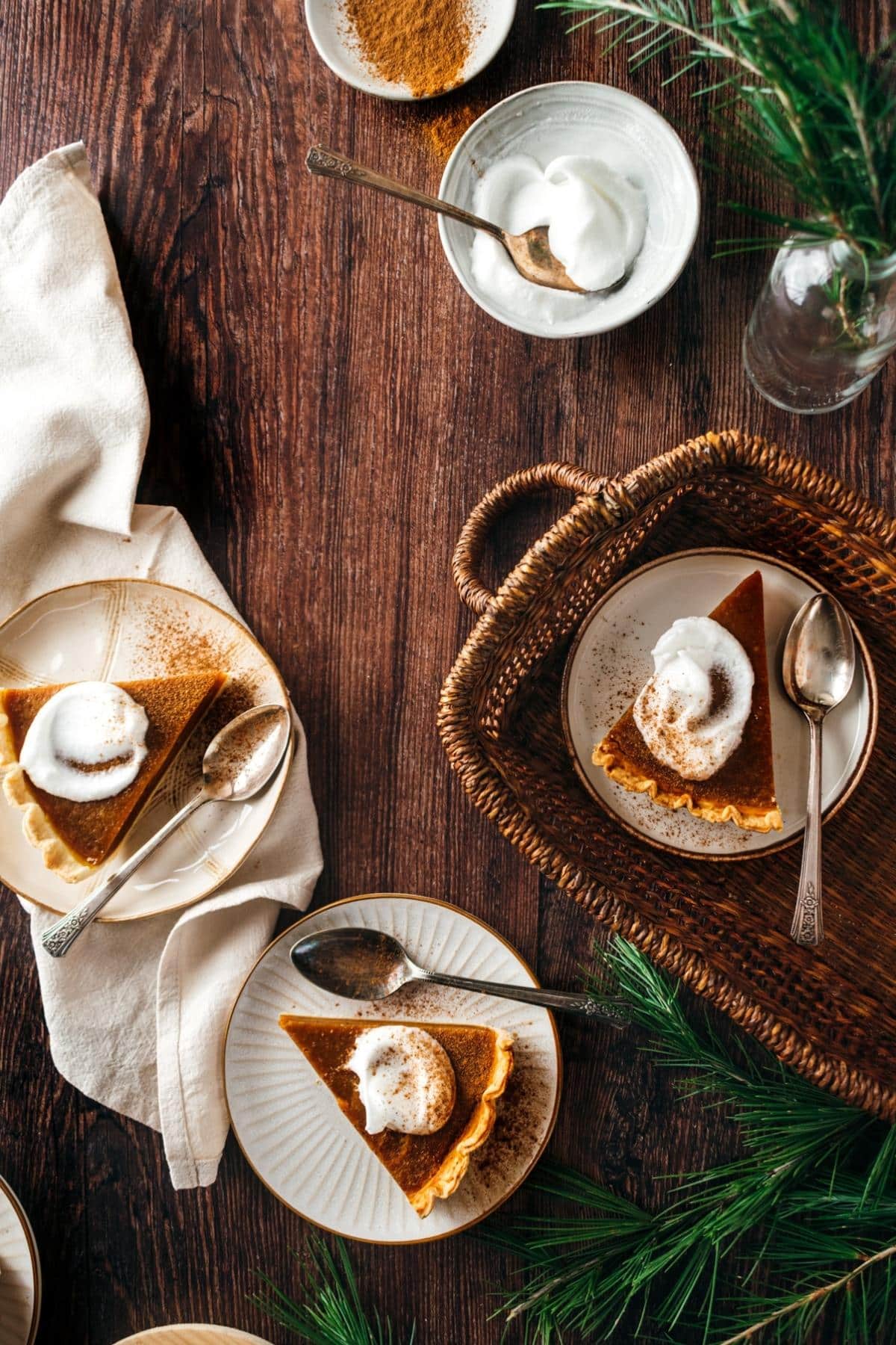 Slices of egg-free pumpkin pie with whipped cream, sit on plates accompanied by spoons.