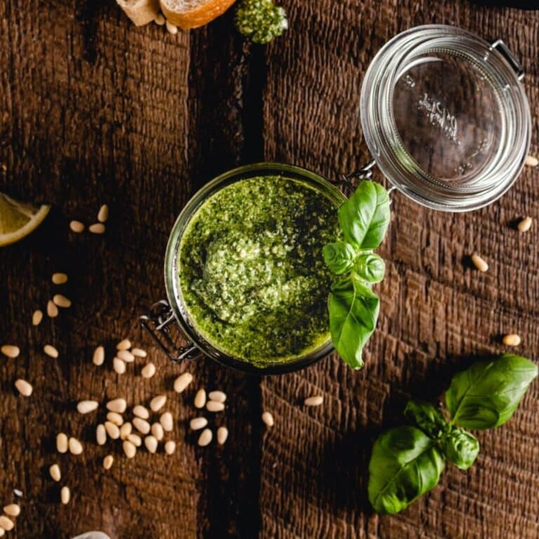 A jar of vibrant pesto with a basil garnish on a wooden table.
