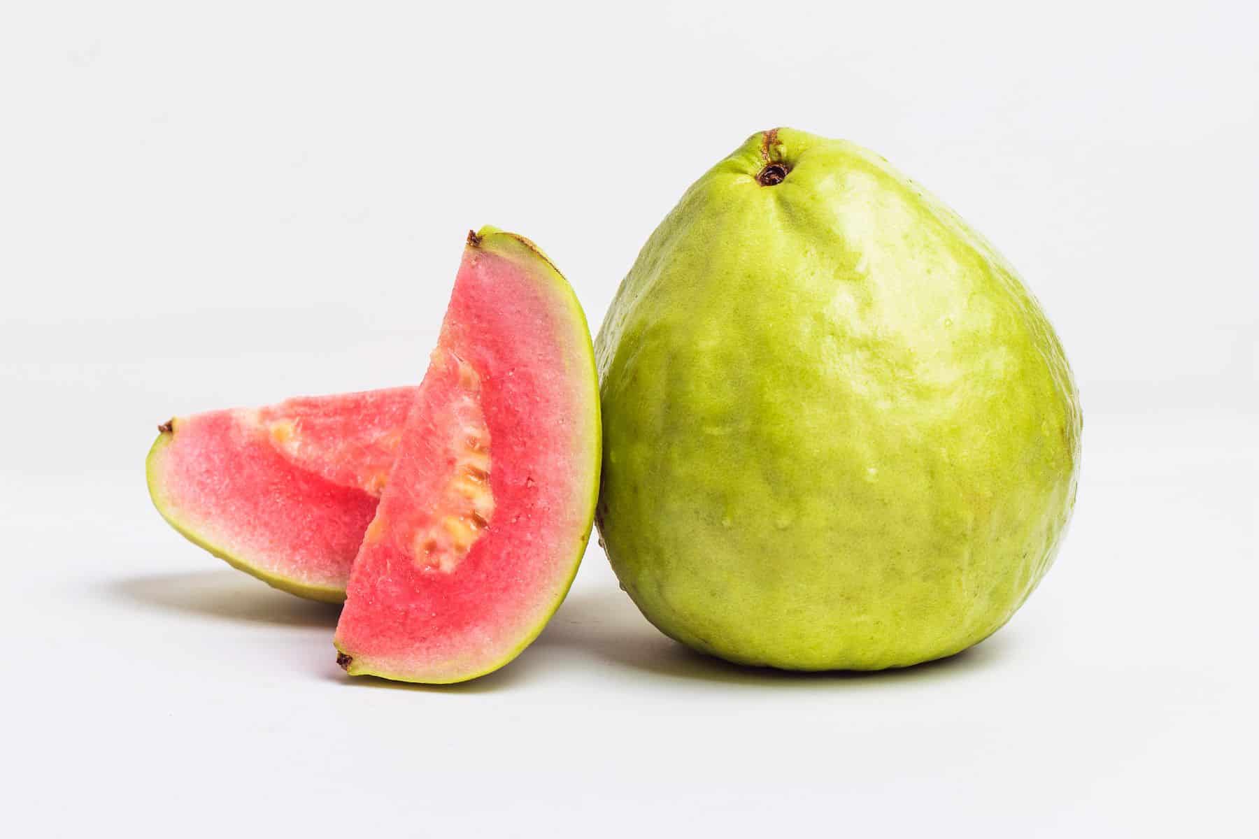 A whole guava and two slices are displayed against a white background.