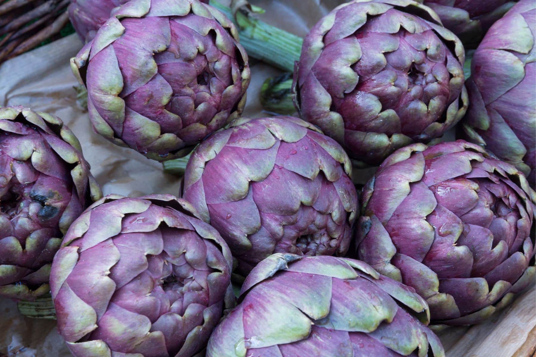 Purple artichokes piled together on a wooden surface.