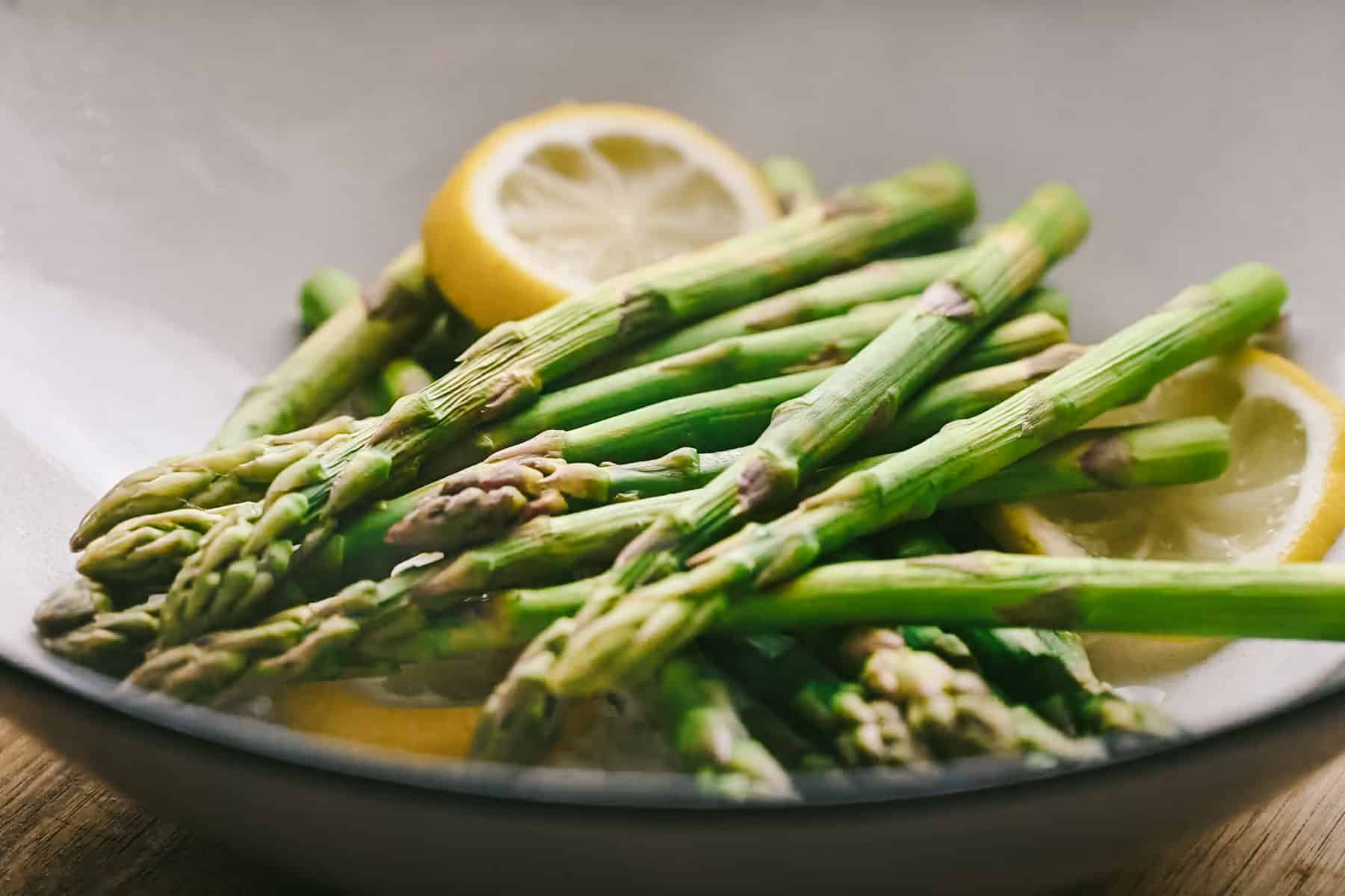 A bowl of cooked asparagus spears with lemon slices.