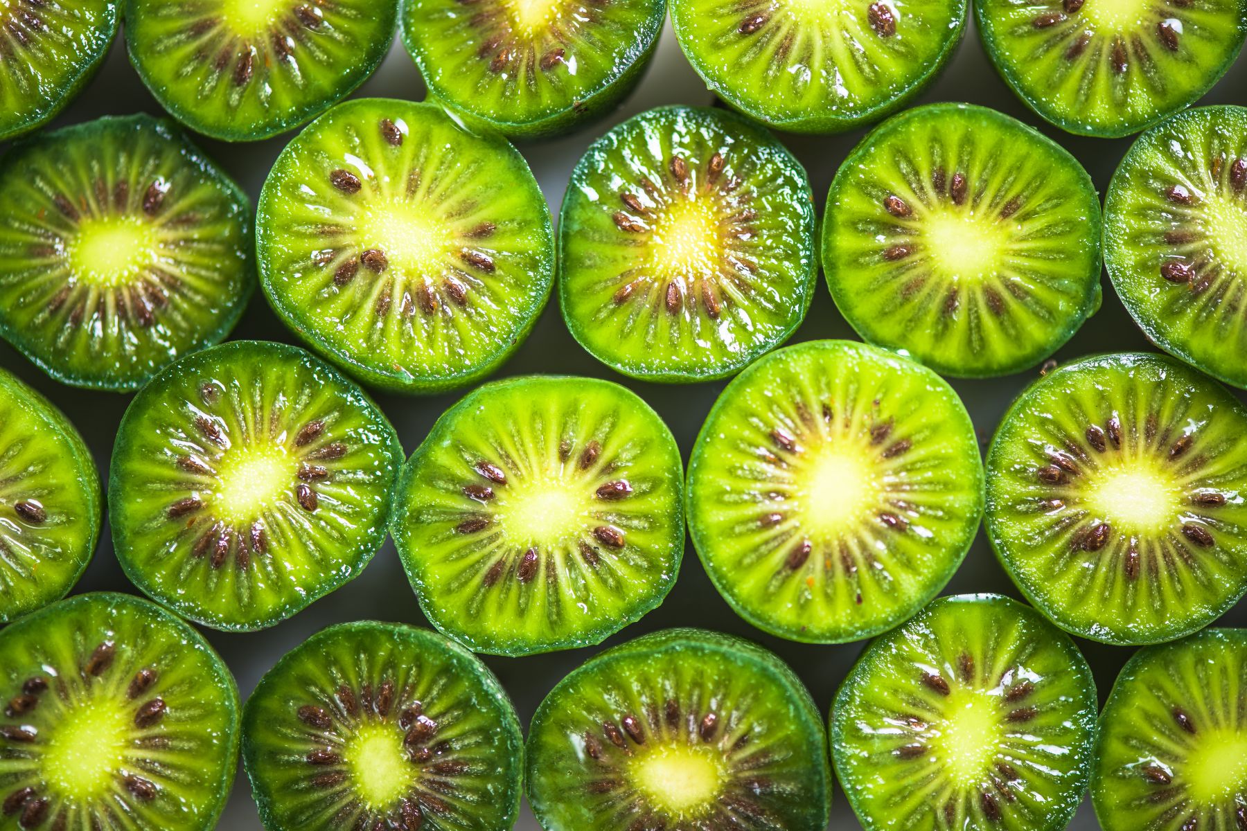 Close-up of sliced green kiwiberry halves arranged in rows, displaying seeds and vibrant green flesh.