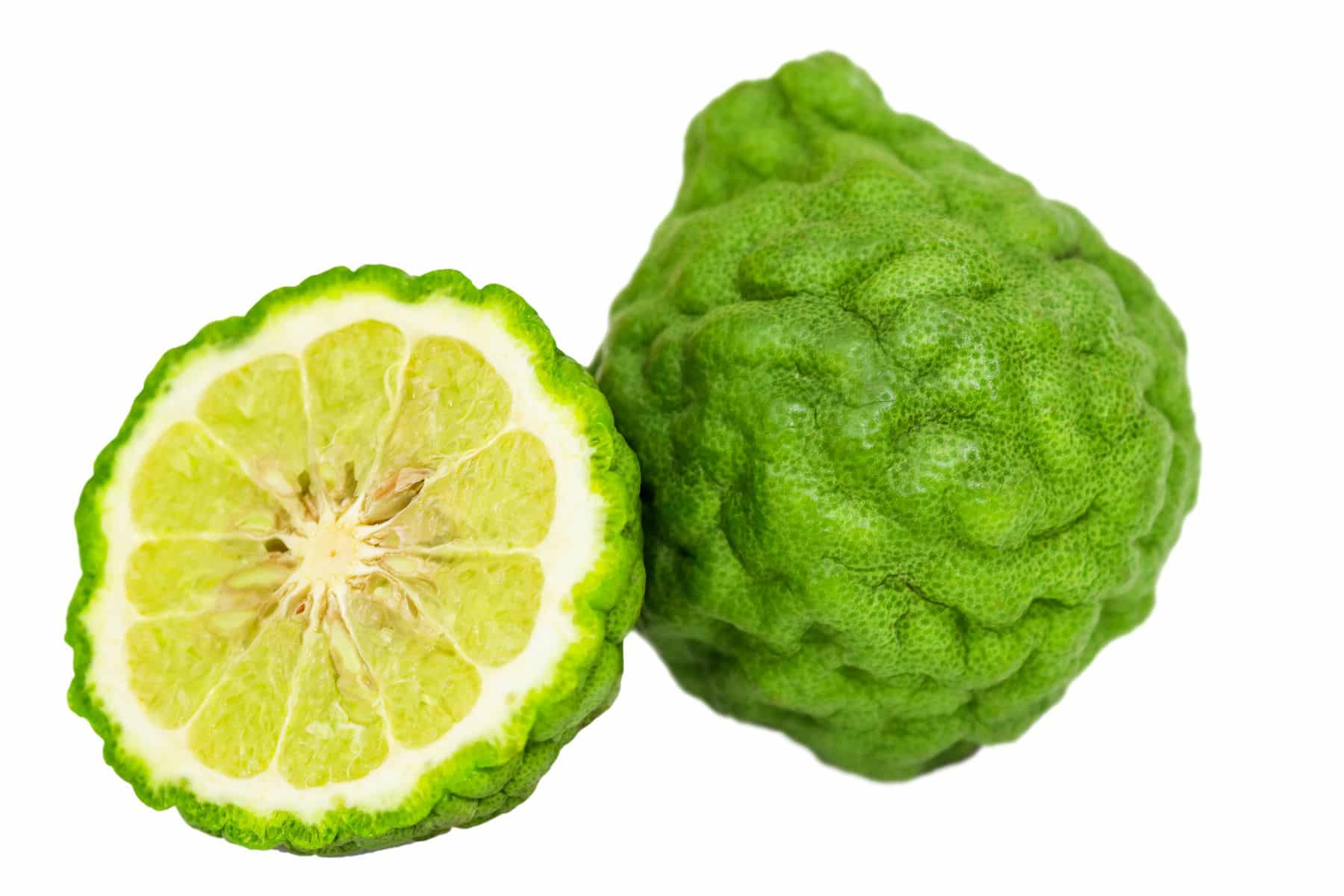 Two bergamot fruits, one whole and one cut in half, displaying green bumpy skin and interior citrus segments, on a white background.