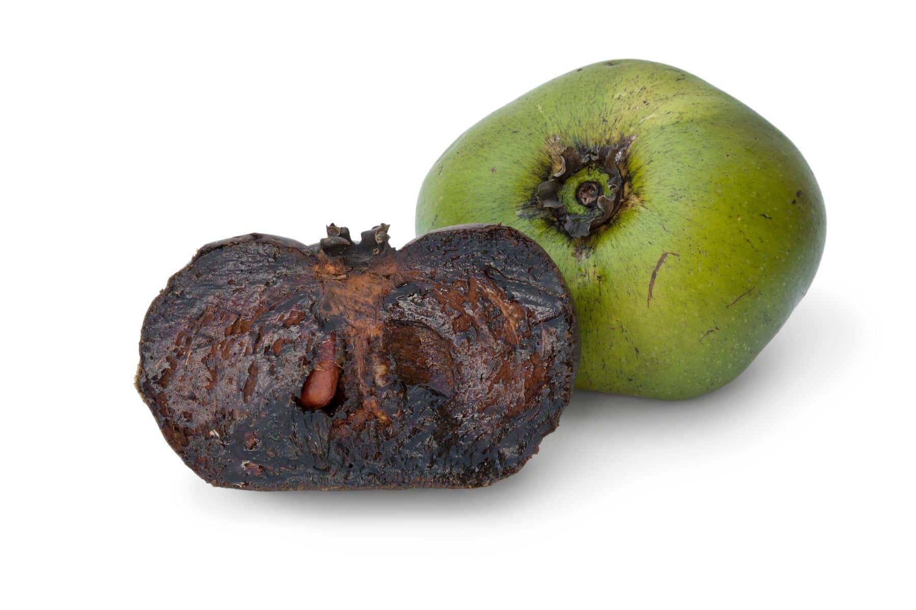 Whole and halved black sapote fruit on a white background. The halved fruit shows a dark brown interior.