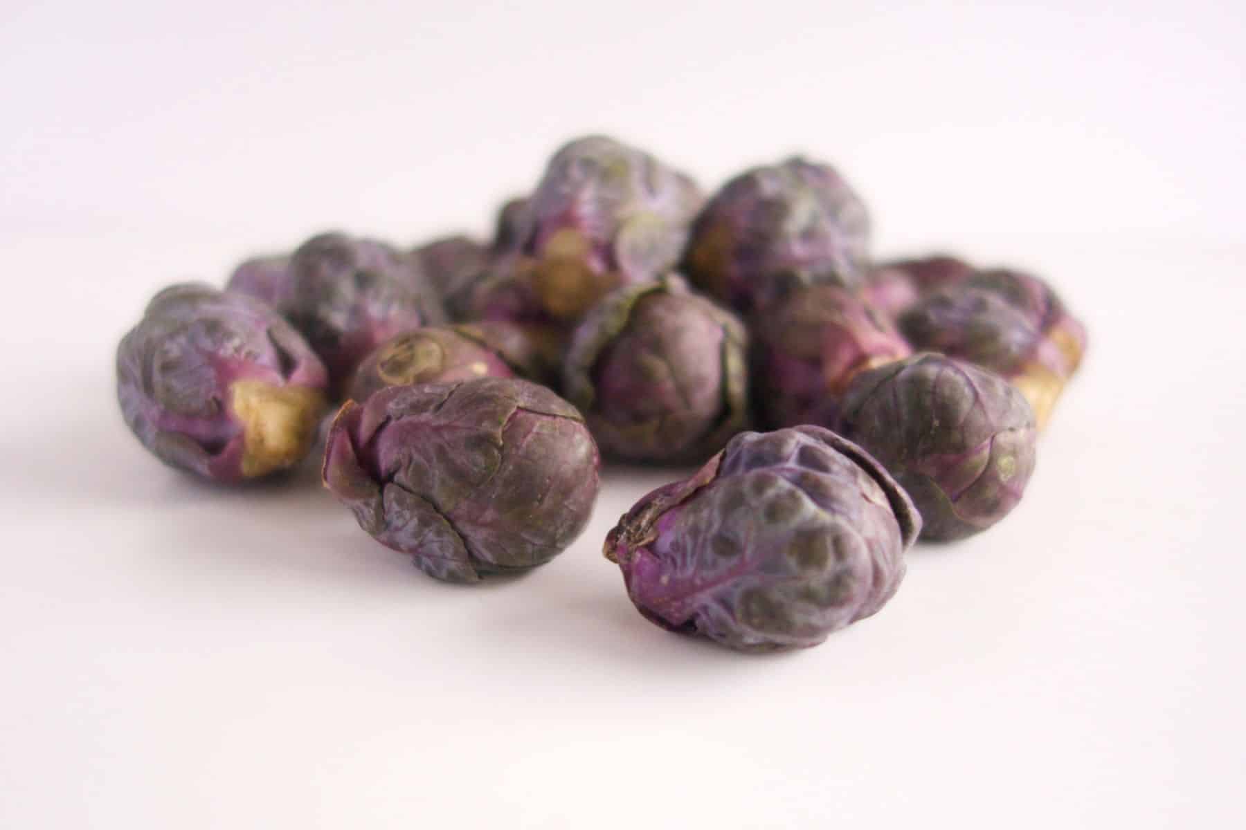 Purple Brussels sprouts scattered on a white surface.