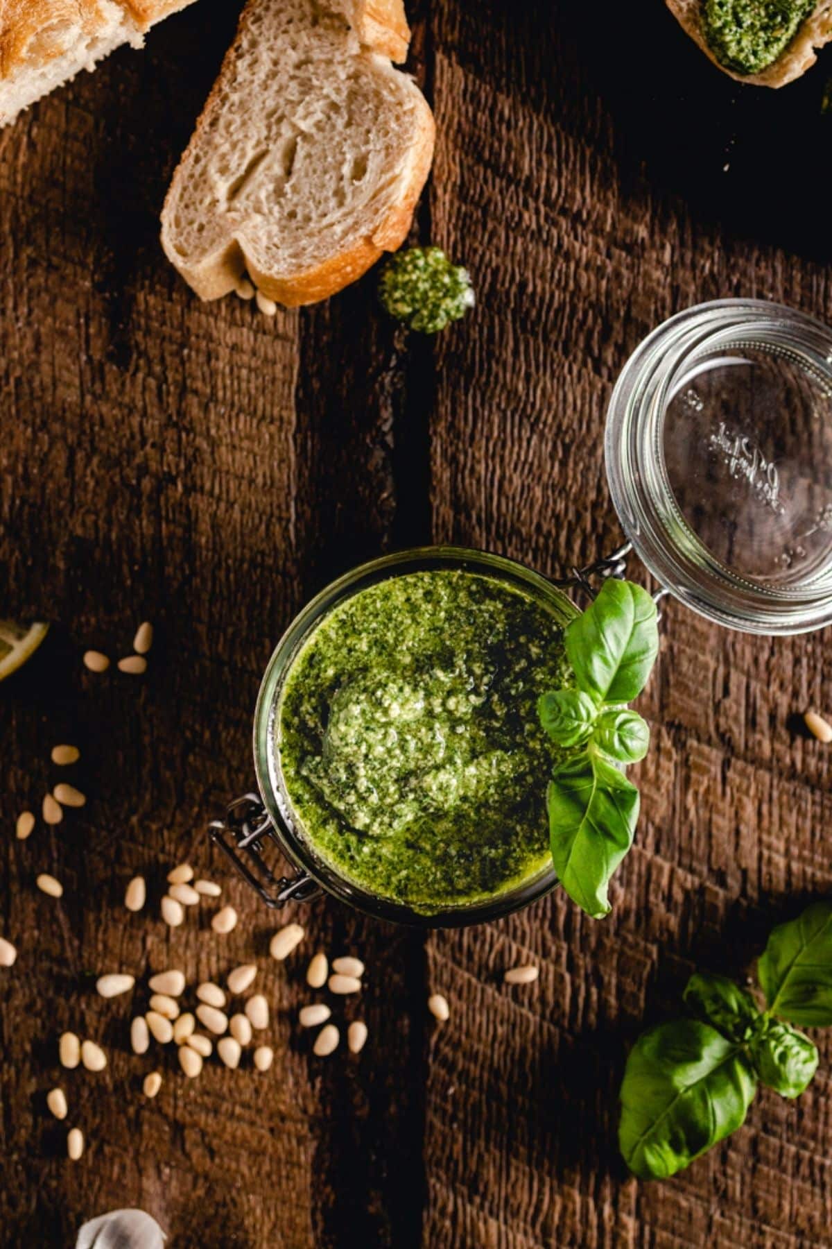 A jar of green pesto with a basil garnish on a wooden surface.