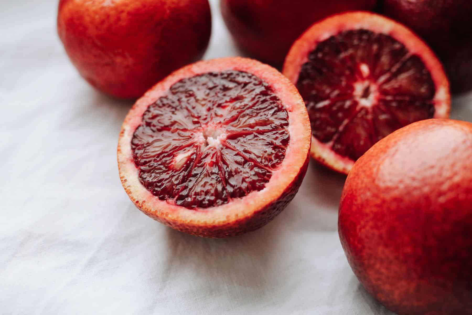 Halved and whole blood oranges on a white surface.