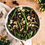 A bowl of fresh green beans is artfully garnished with sliced almonds and tart cranberries.