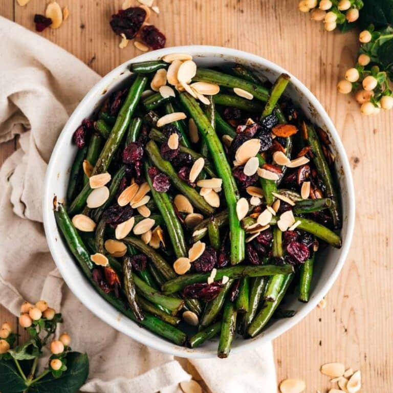 A bowl of fresh green beans is artfully garnished with sliced almonds and tart cranberries.
