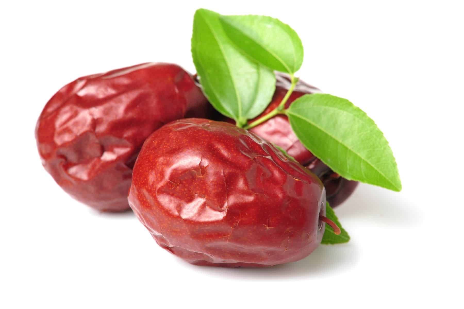 Three ripe red jujubes with green leaves on a white background.