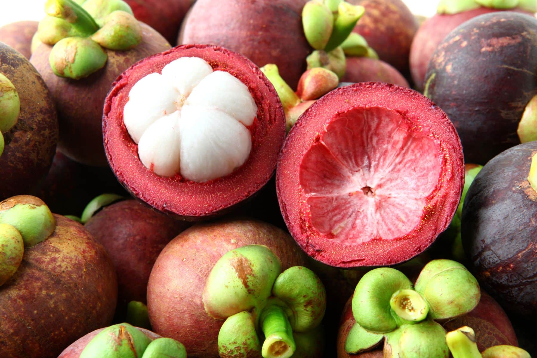 A pile of mangosteens with a few cut open, displaying white segmented flesh.