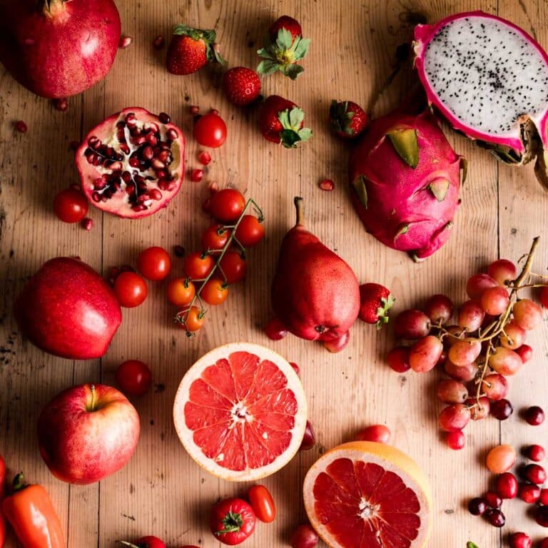A variety of fruits including pomegranate, dragon fruit, strawberries, apples, grapes, grapefruit, tomatoes, and pears on a wooden surface.