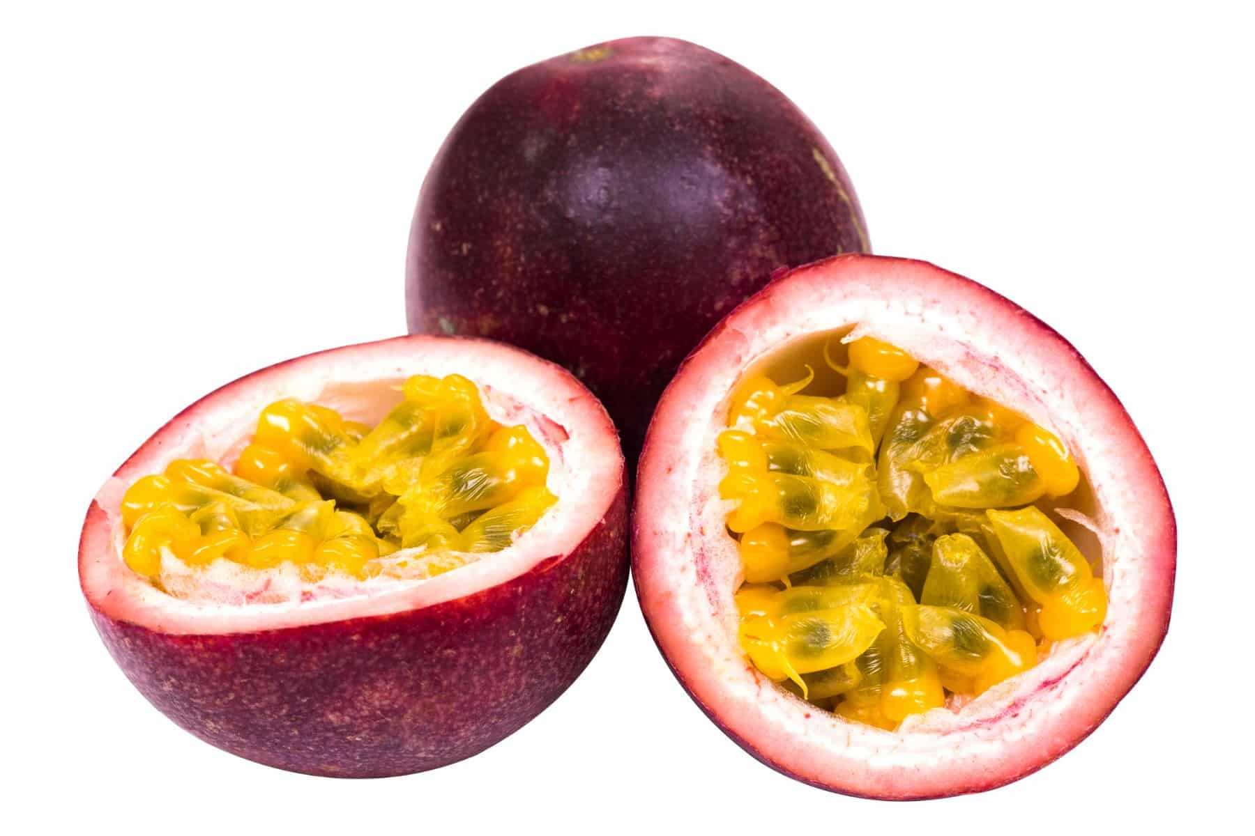 Whole and halved passion fruits with purple skin and yellow, seedy pulp on a white background.