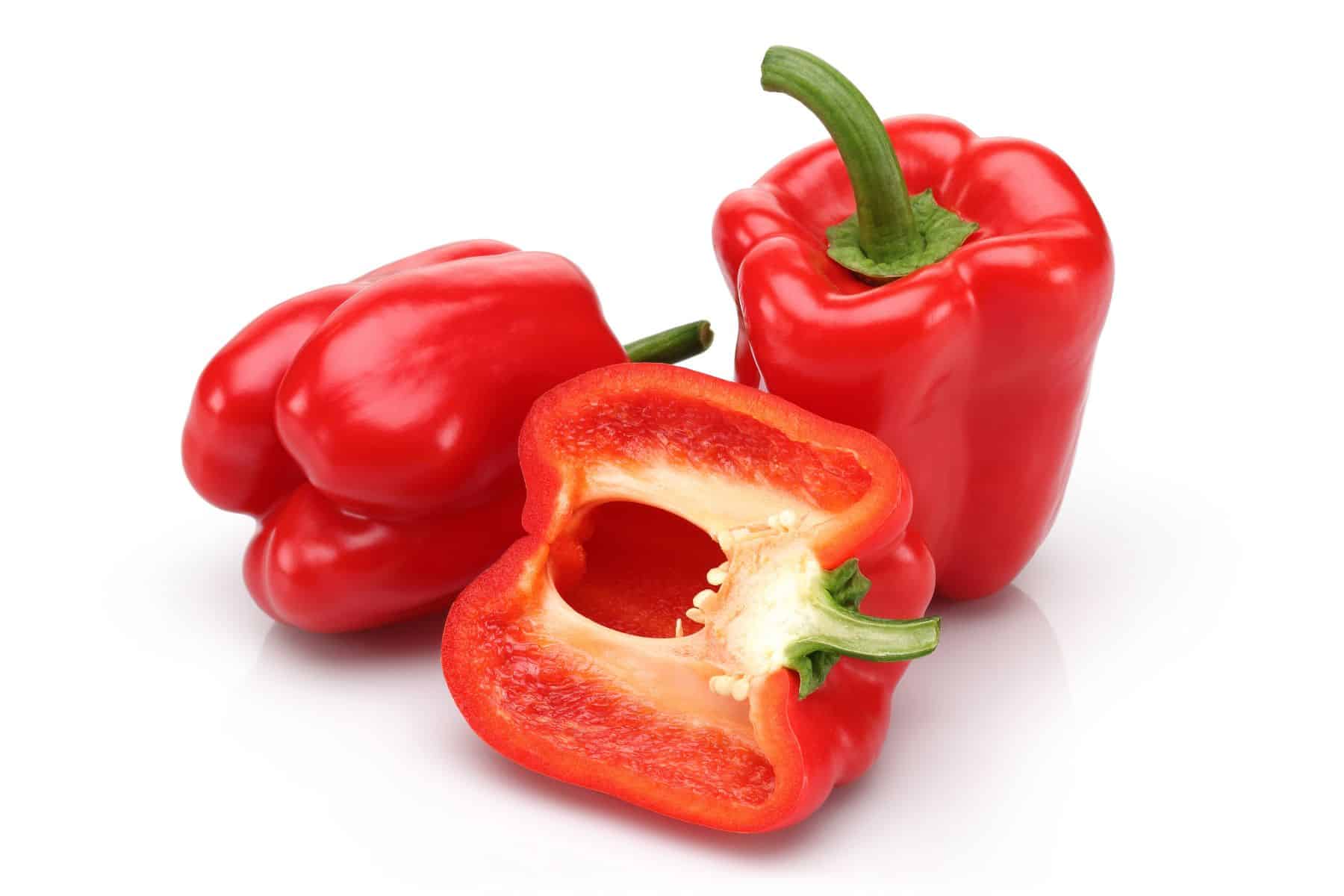 Three vibrant red bell peppers are displayed: two whole and one sliced in half, revealing seeds and the interior. The background is plain white.