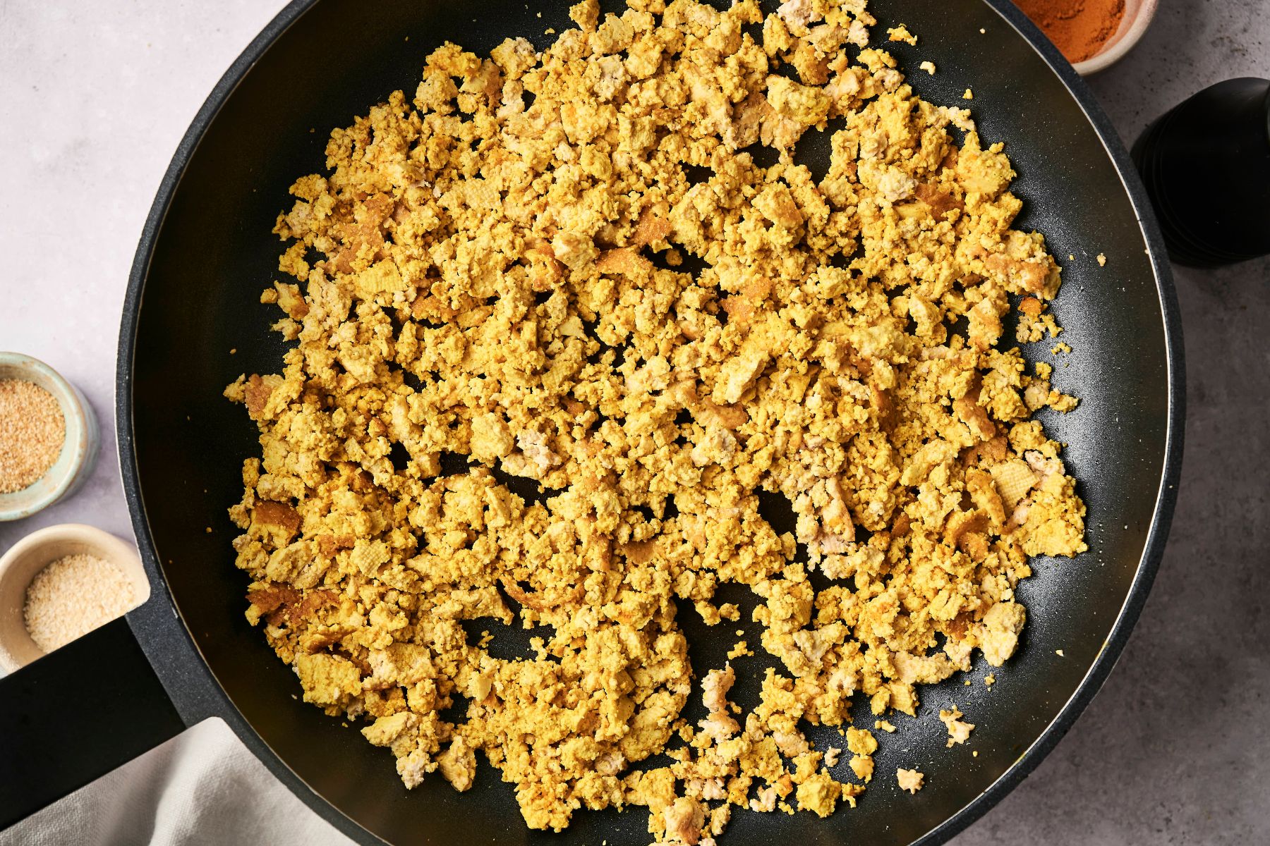 A frying pan filled with cooked, crumbled tofu seasoned with spices.