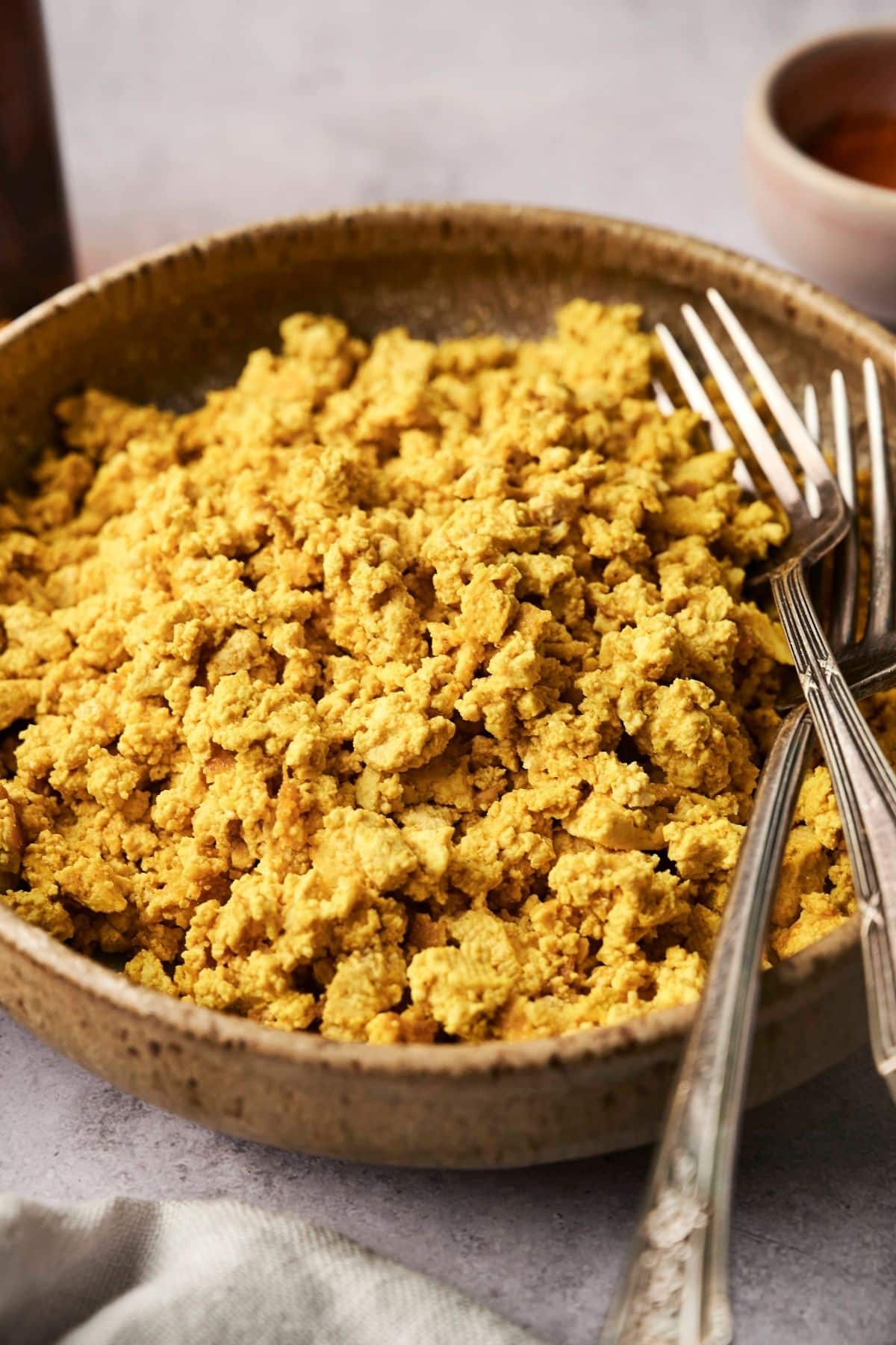 A bowl of scrambled tofu on a table, with three forks resting on the side.