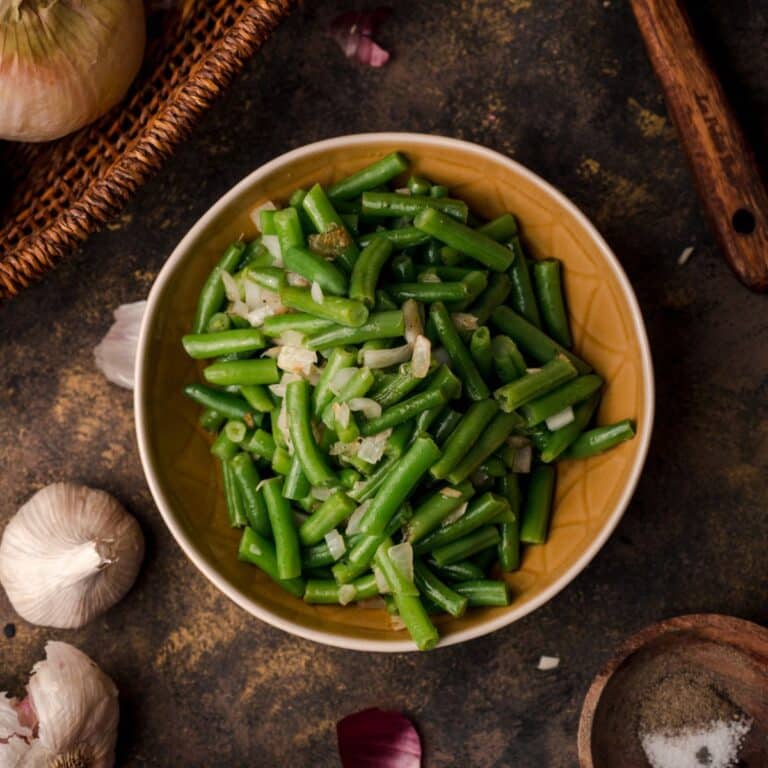 Cooked canned green beans with onion and garlic in a serving bowl.