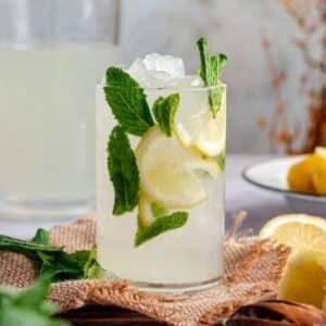 Glass of lemonade with fresh mint and lemon wedges.