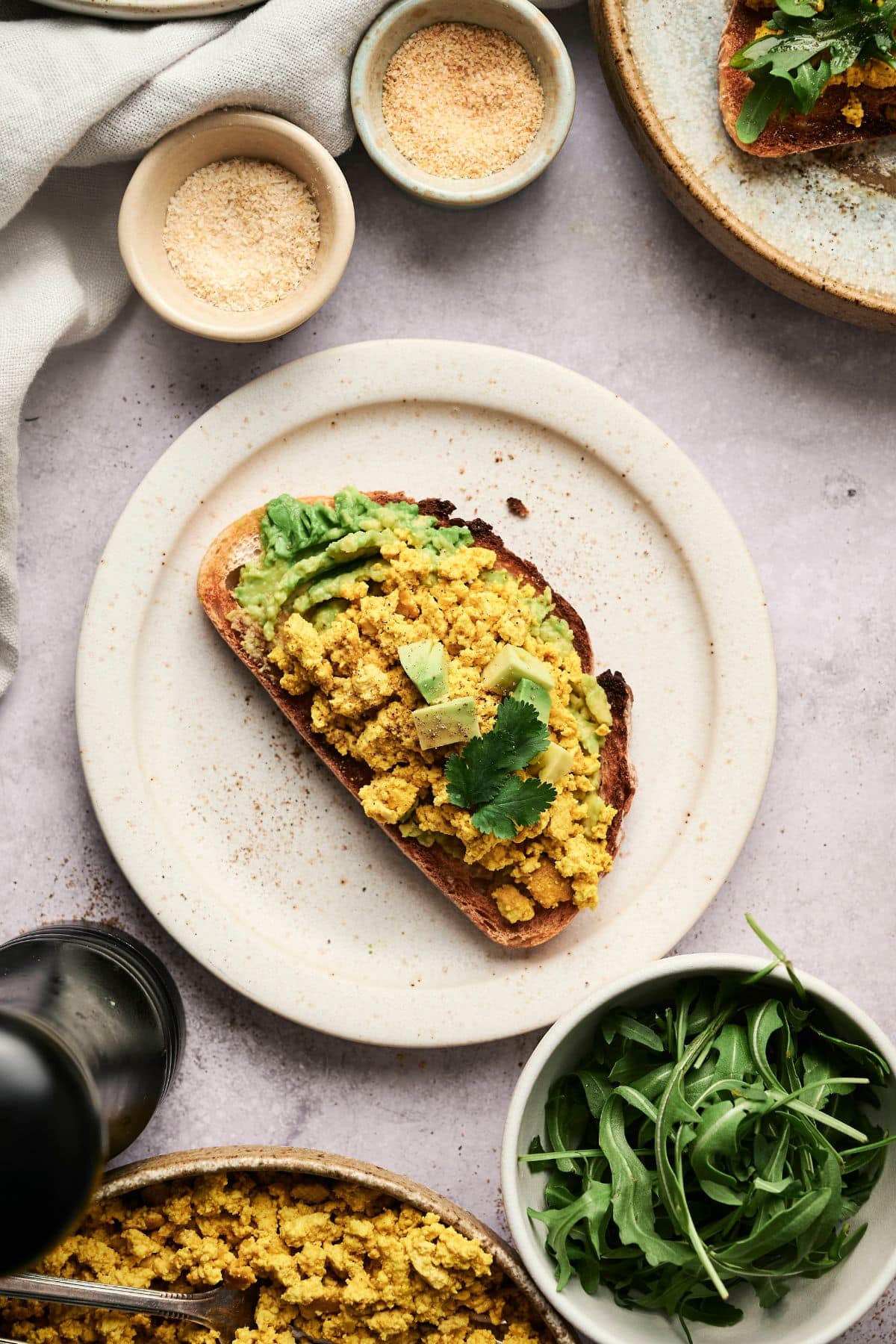 Scrambled tofu on top of mashed avocado on toast with fresh green herb sprig on top.