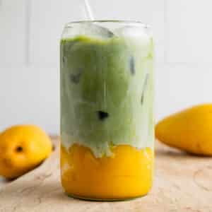 Mango matcha latte in a clear glass cup with fresh mangoes next to it.