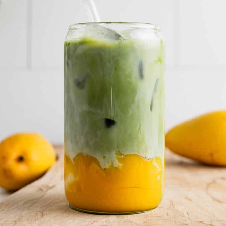 Mango matcha latte in a clear glass cup with fresh mangoes next to it.