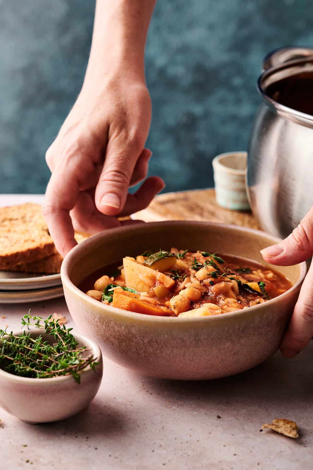 Woman placing a bowl of cozy orzo veggie soup on the table.
