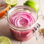 Homemade lime picked onions in a clear glass jar with a glass lid and metal clasp.