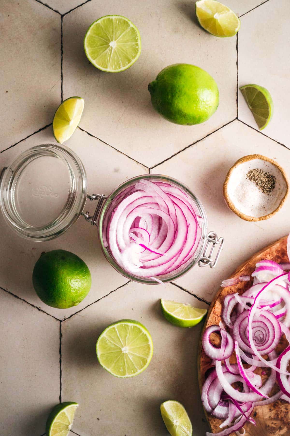Red onions being added to a clear glass jar.
