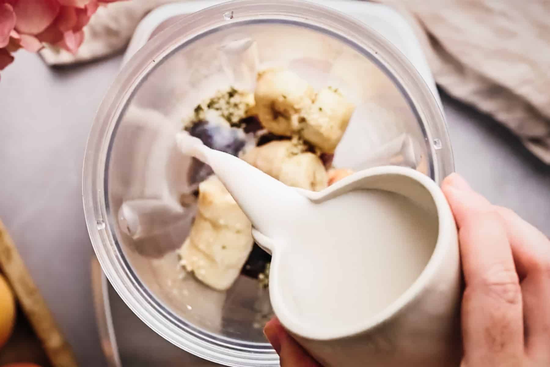 Pouring milk over frozen fruit in a blender.