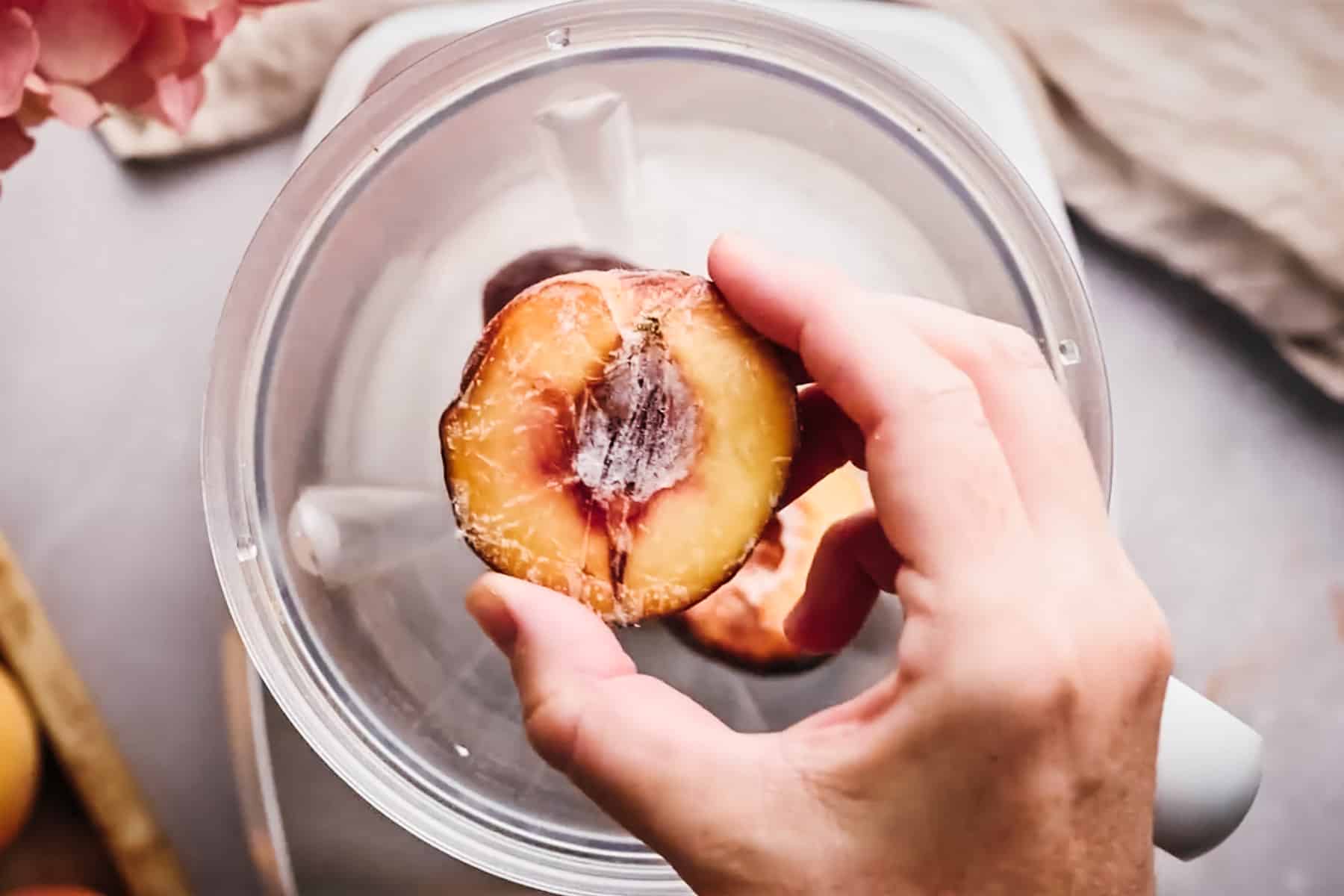 Adding frozen peaches to a blender.