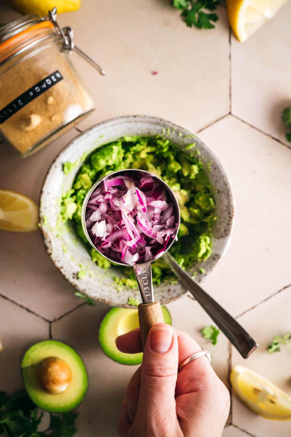 Red onion being added to a bowl of mashed avocado.