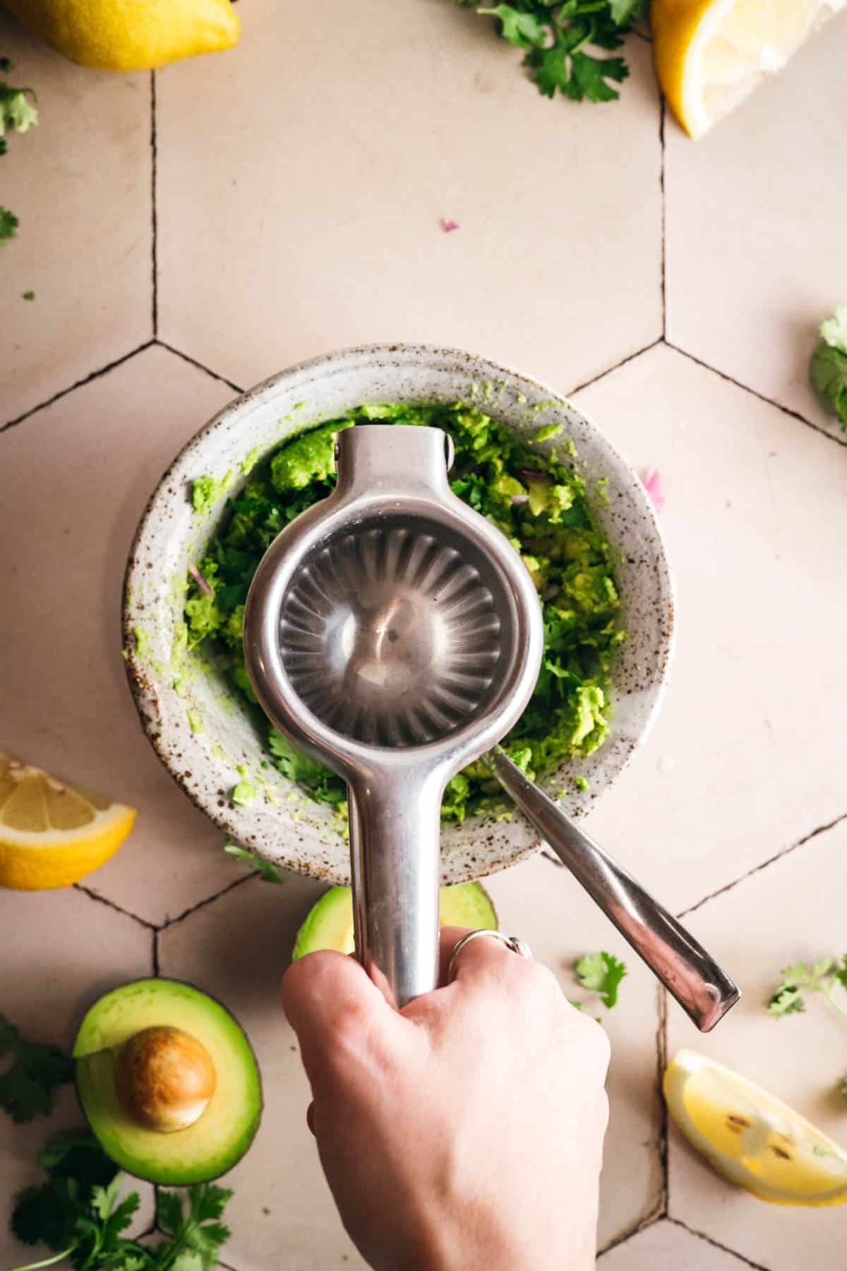 Squeezing fresh lemon juice into a bowl of avocado, spices, and herbs.