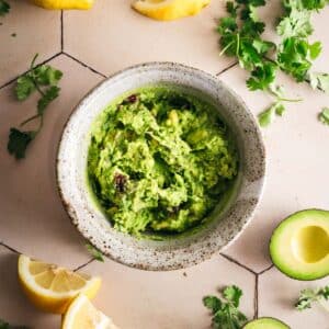 Fresh homemade guacamole with avocado, lemon and herbs on a tile counter.