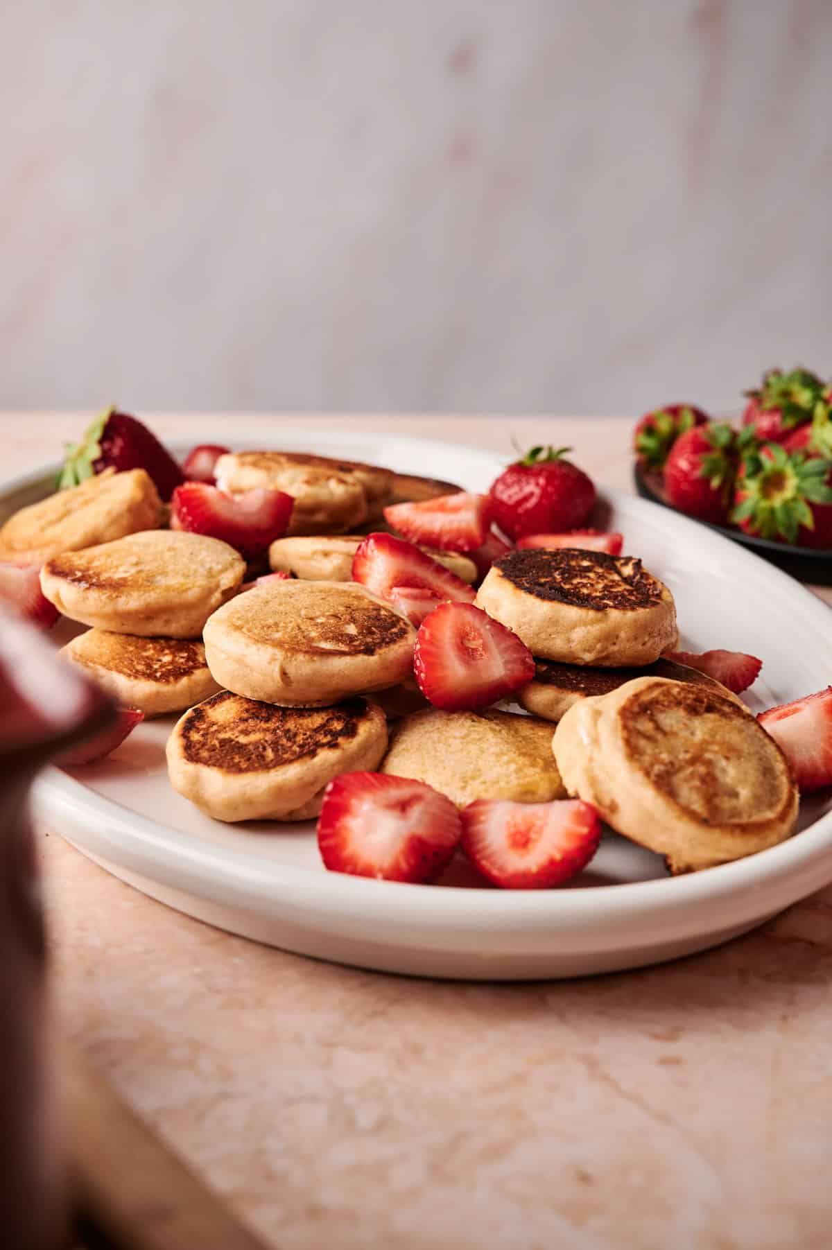 Shaking powdered sugar on top of mini pancakes on an oval plate.