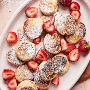 Close up of tiny pancakes with fresh berries and powdered sugar on top.