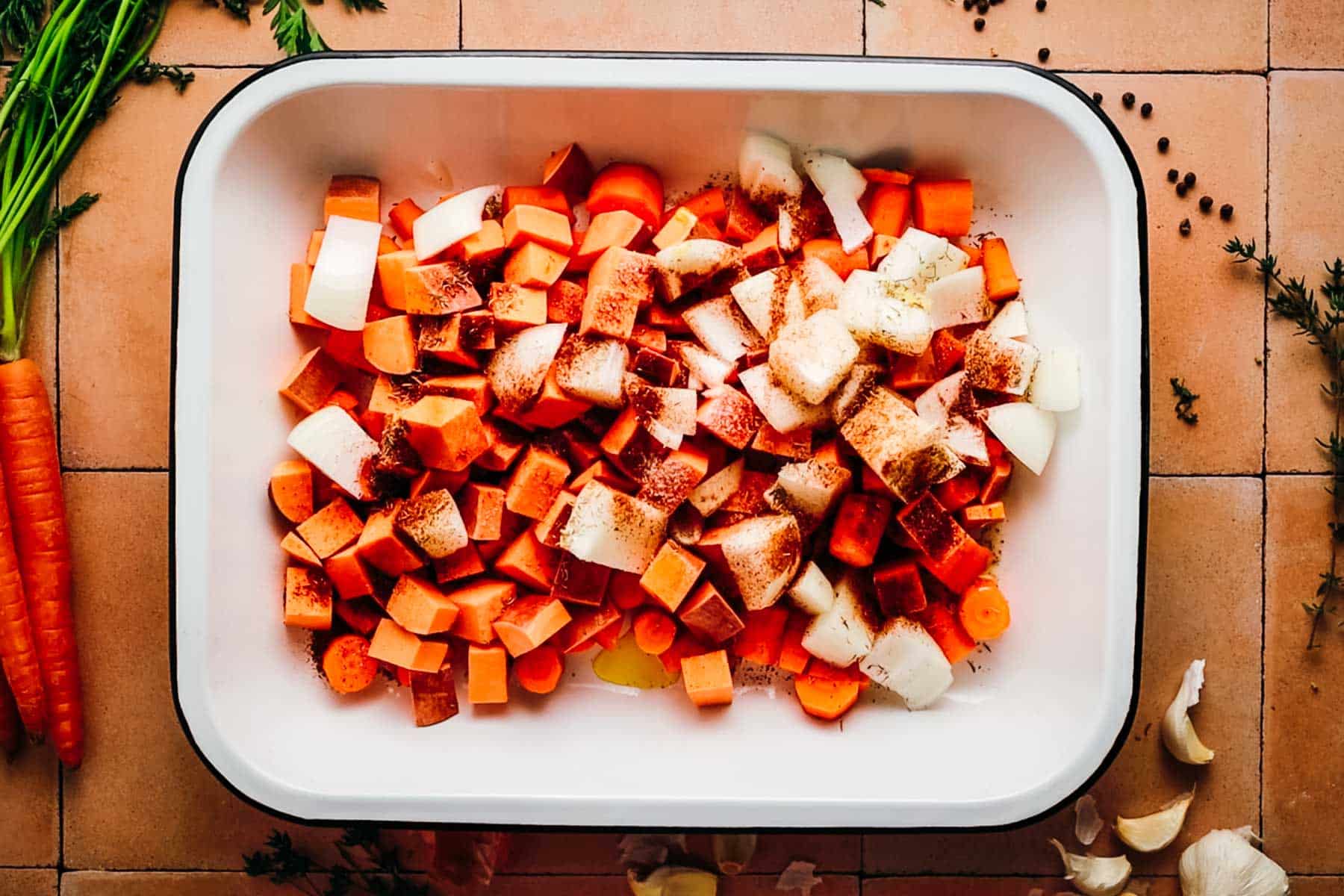Pepper and spices added on top of root vegetables in a baking dish.