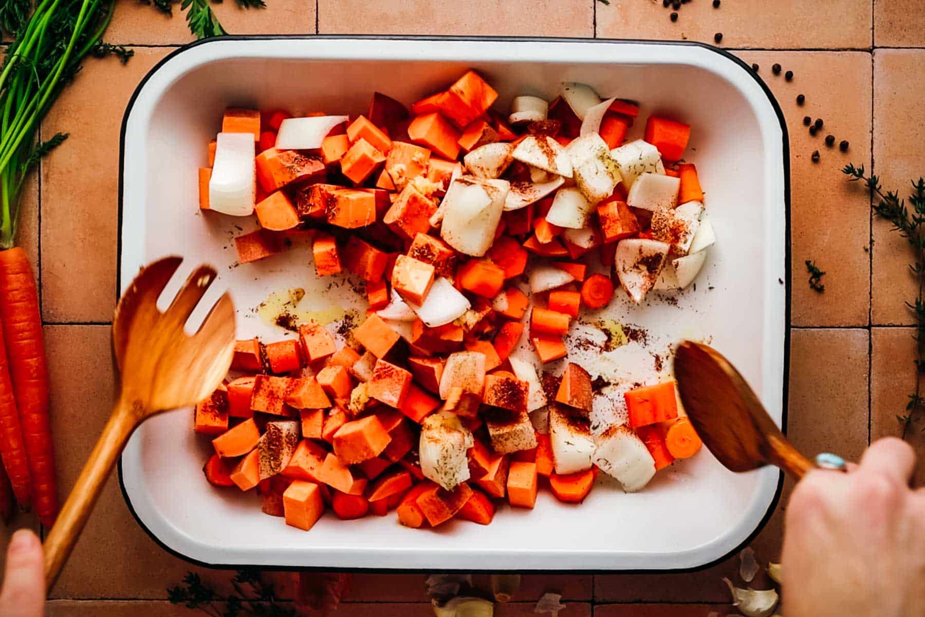 Woman mixing chopped carrots, sweet potatoes, and seasonings together.