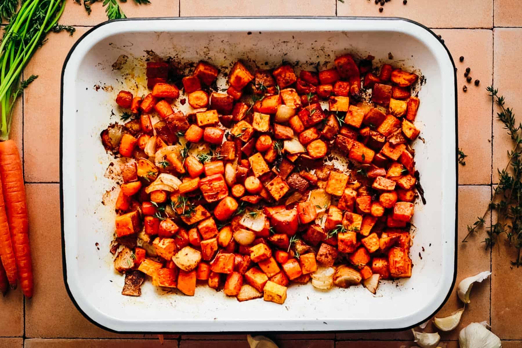 Roasted sweet potatoes and carrots in an enamel baking tray on a clay top table.