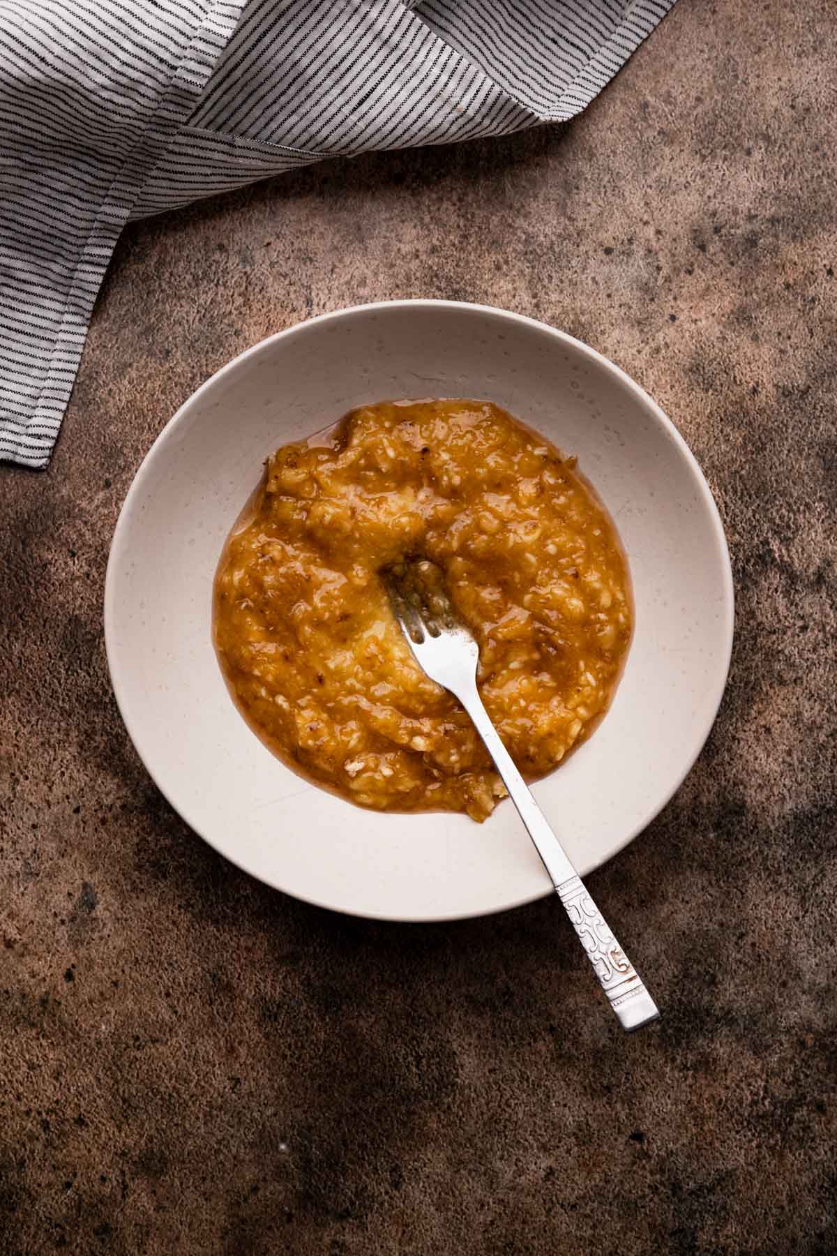 Mashing the banana in a shallow white bowl.