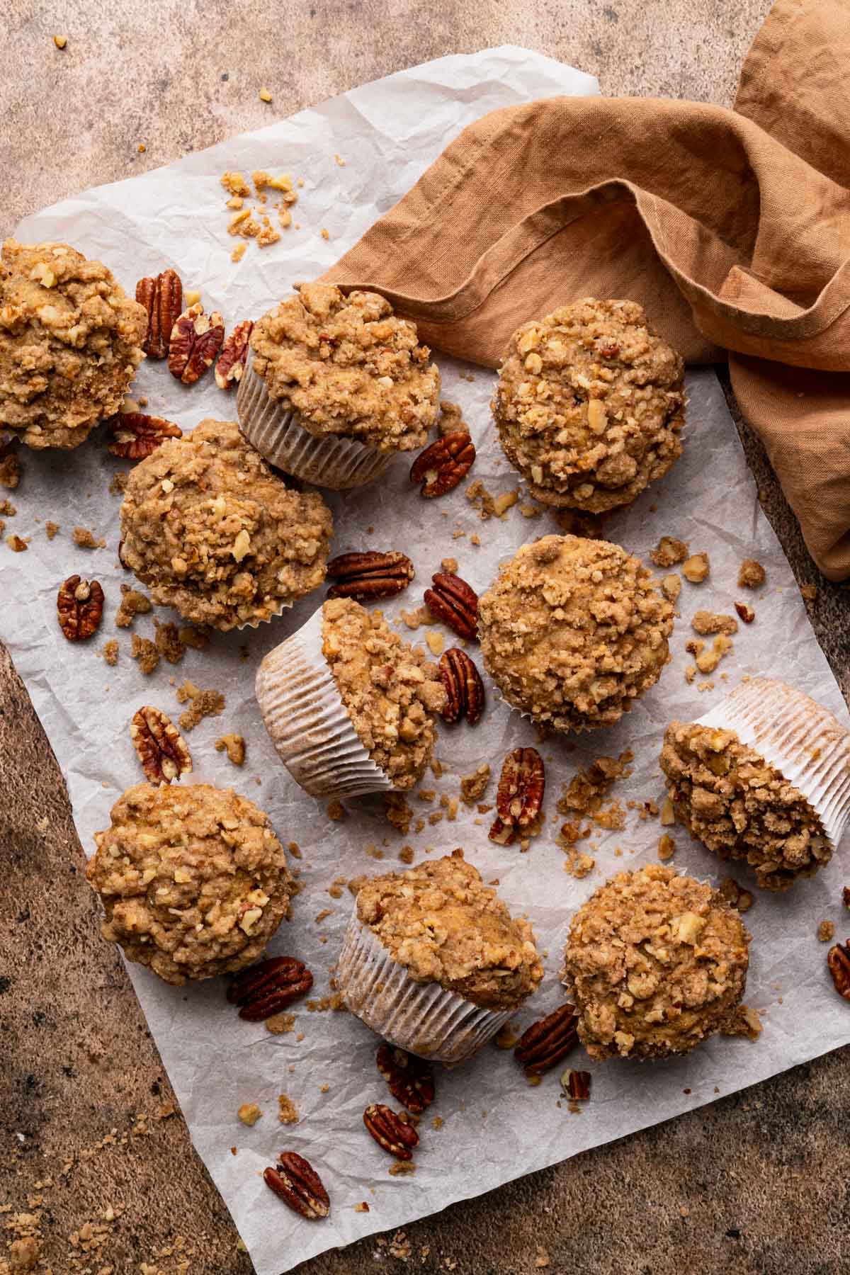 Fresh muffins on a rectangle piece of parchment paper with pecans around.