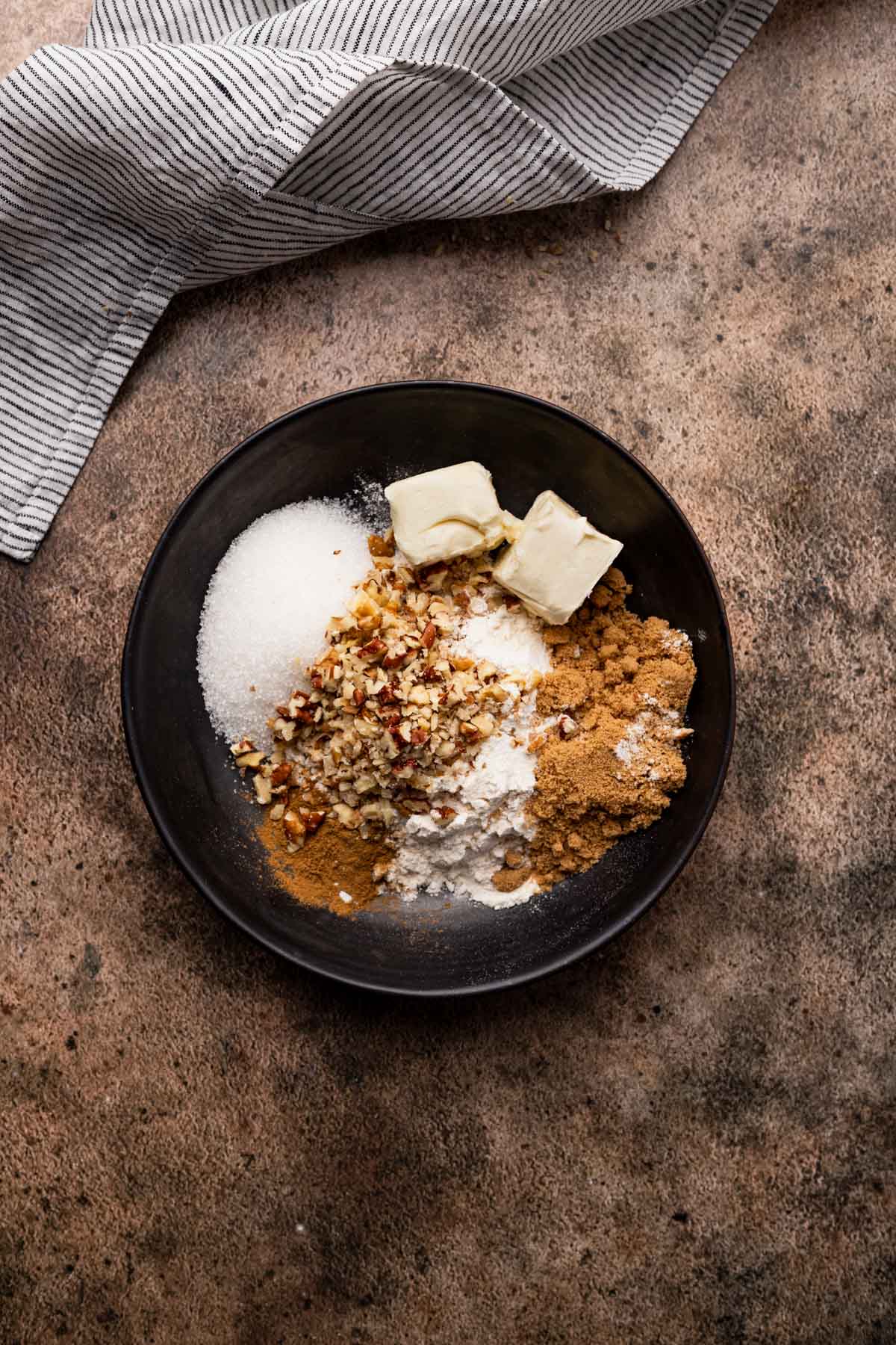 Combining streusal topping ingredients in a shallow black ceramic bowl.