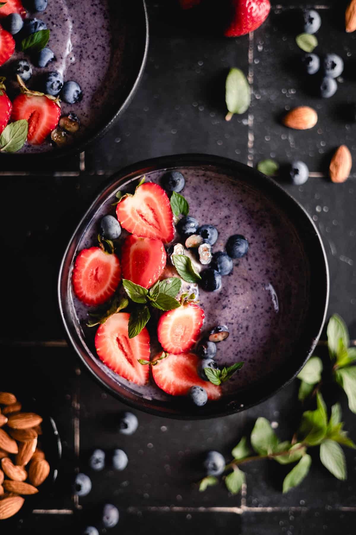 Vibrant blueberry smoothie in a black bowl with fresh berries on top.